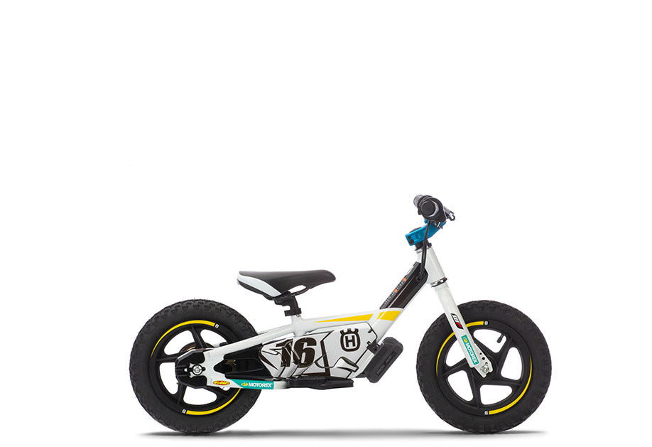 A Stacyc 12eDRIVE Husqvarna Factory Replica riding toy bike with white, black, and yellow color scheme, featuring 12-inch wheels and a battery compartment.